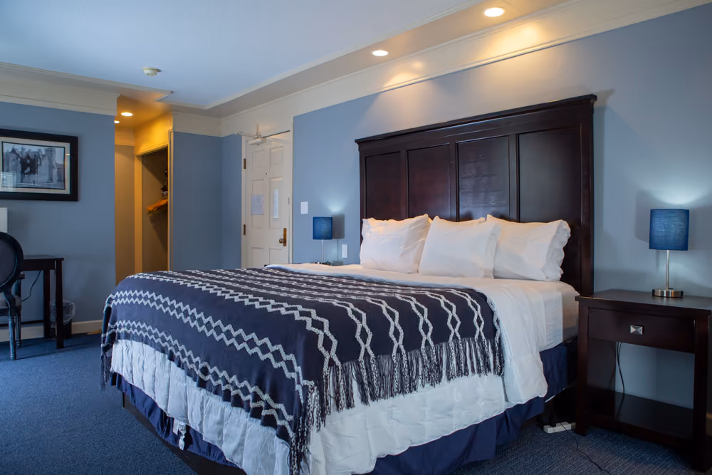 King guest room with dark wood headboard, white bedding, navy patterned throw, nightstands and writing desk