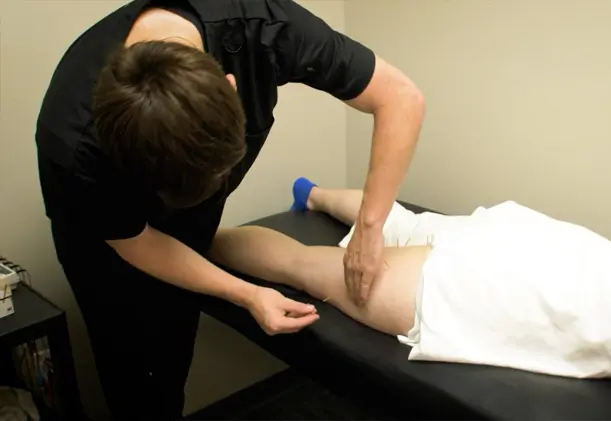 A physical therapist performs dry needling on a patient’s hip and upper thigh while the patient lies on a treatment table.