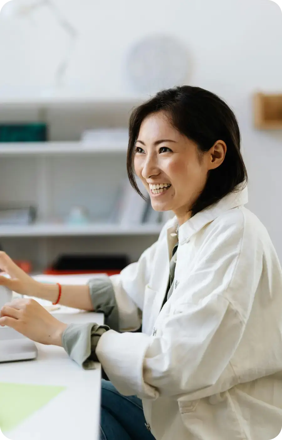 Smiling woman with dark hair wearing a white shirt, sitting at a desk with hands on a laptop keyboard.
