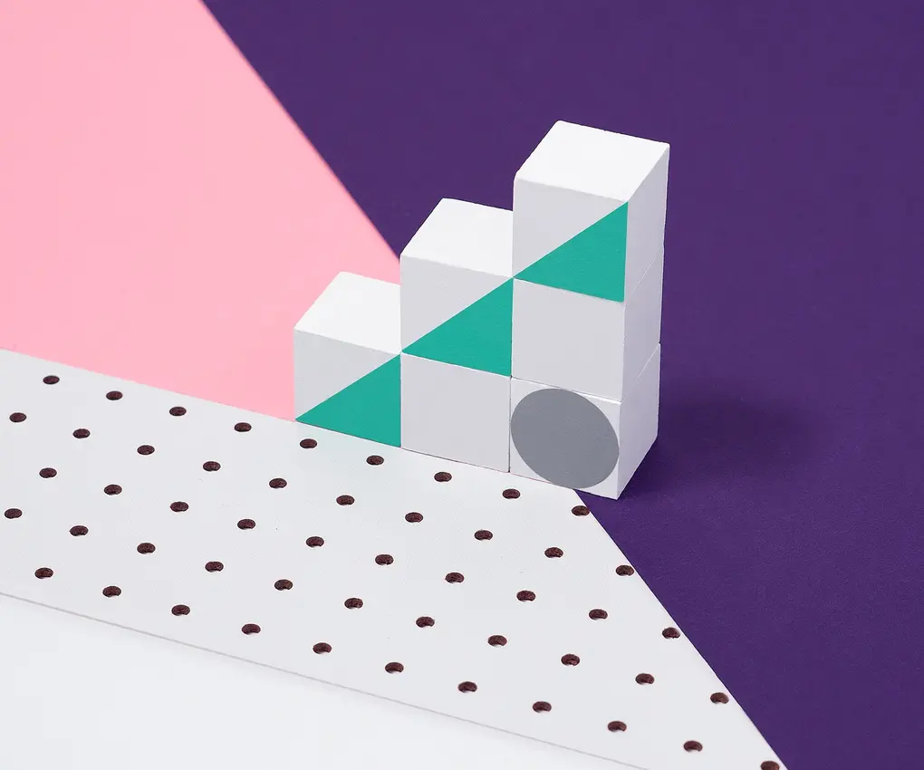 White geometric blocks with teal triangles stacked in a stair shape on purple and pink background.