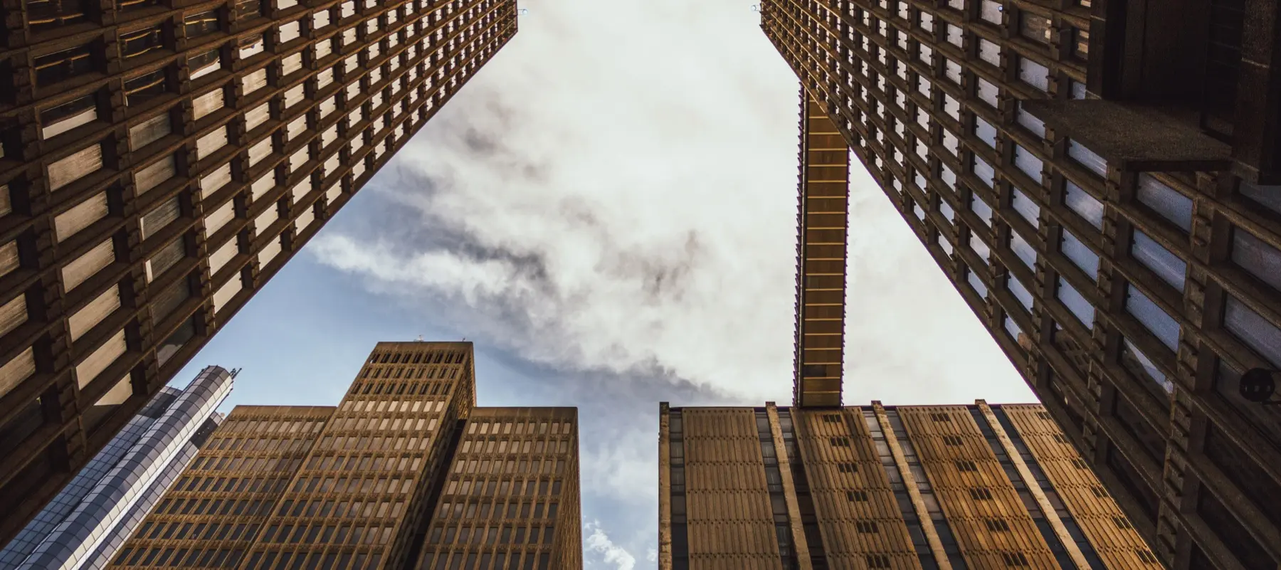 View looking up at tall office buildings with a skybridge connecting two buildings under cloudy sky.