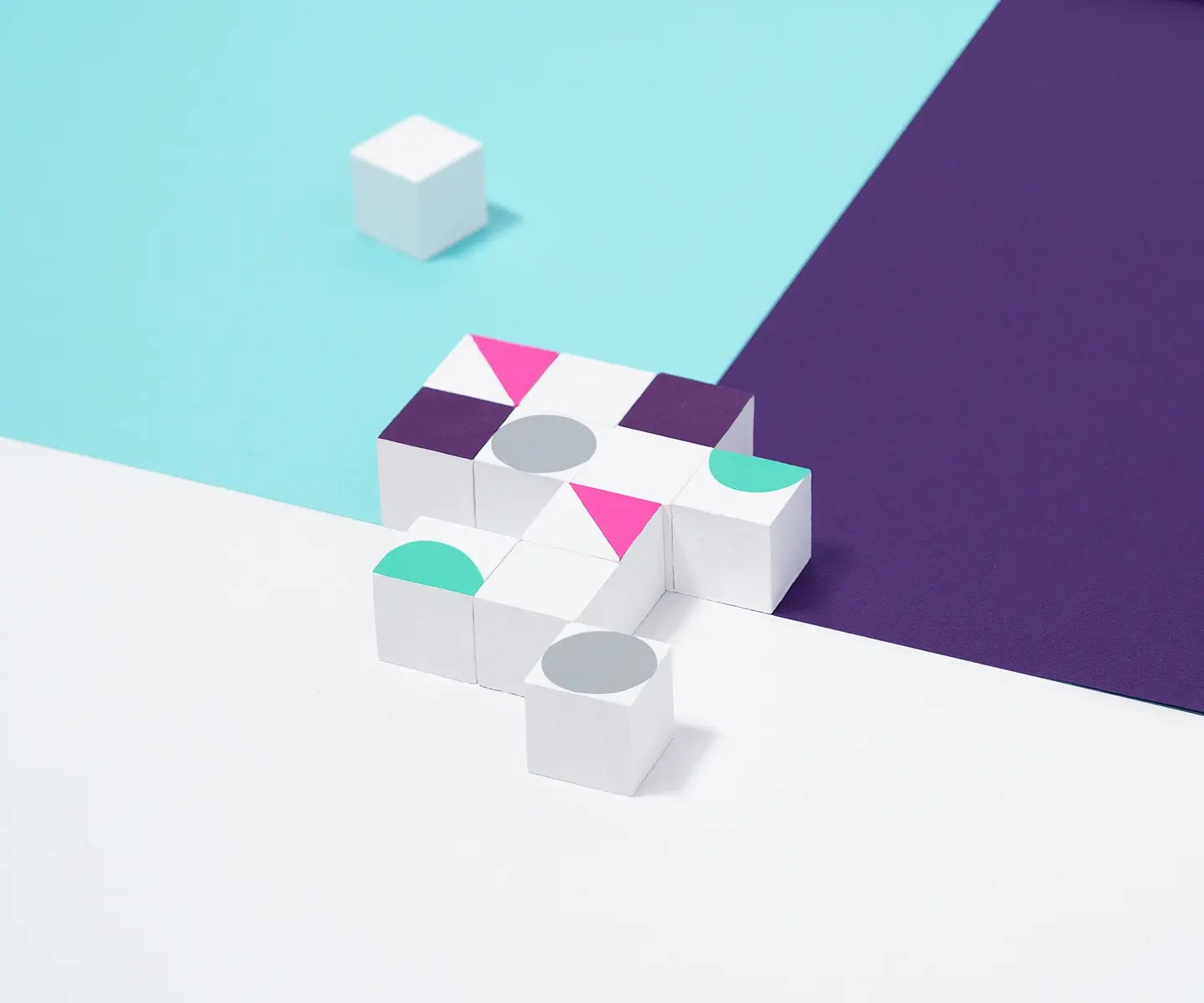 Nine white cubes with colored shapes arranged on a divided surface of white, purple, and blue sections.