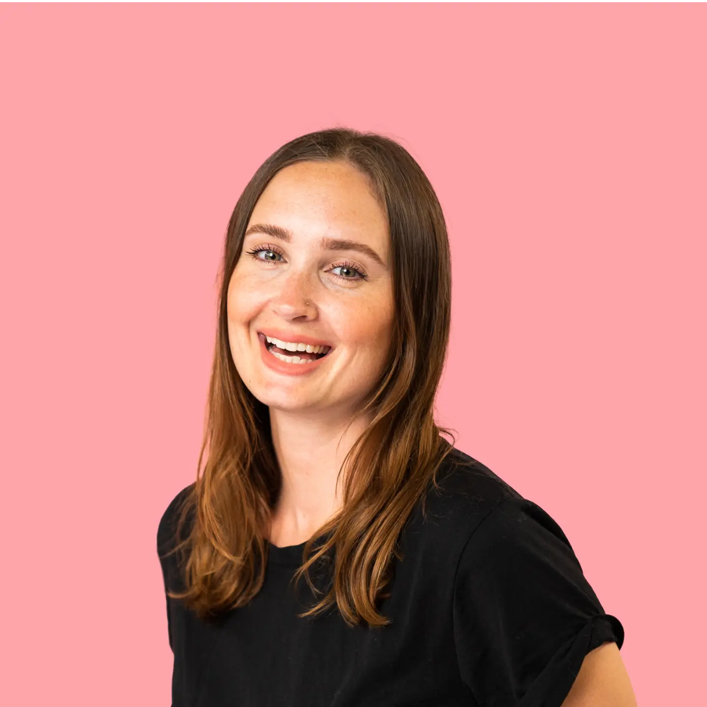 Smiling woman with long brown hair wearing a black shirt against a pink background.