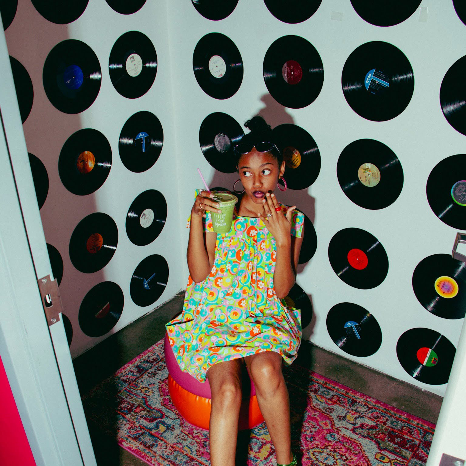 Zariah posing in a room with records on the wall and a hot pink seat with a detailed rug.
