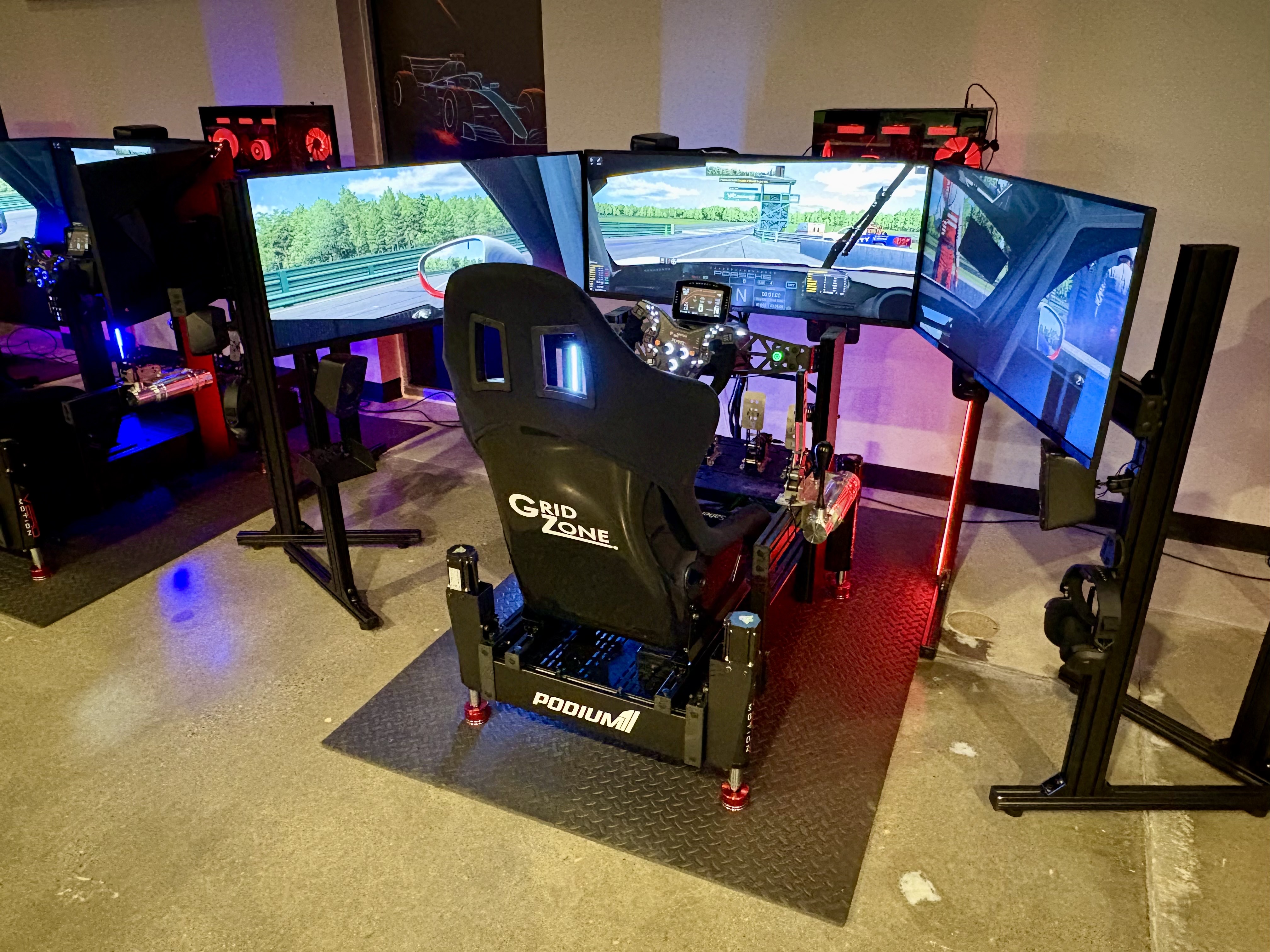 GridZone racing rig with triple monitors, racing seat, steering wheel, and motion platform.
