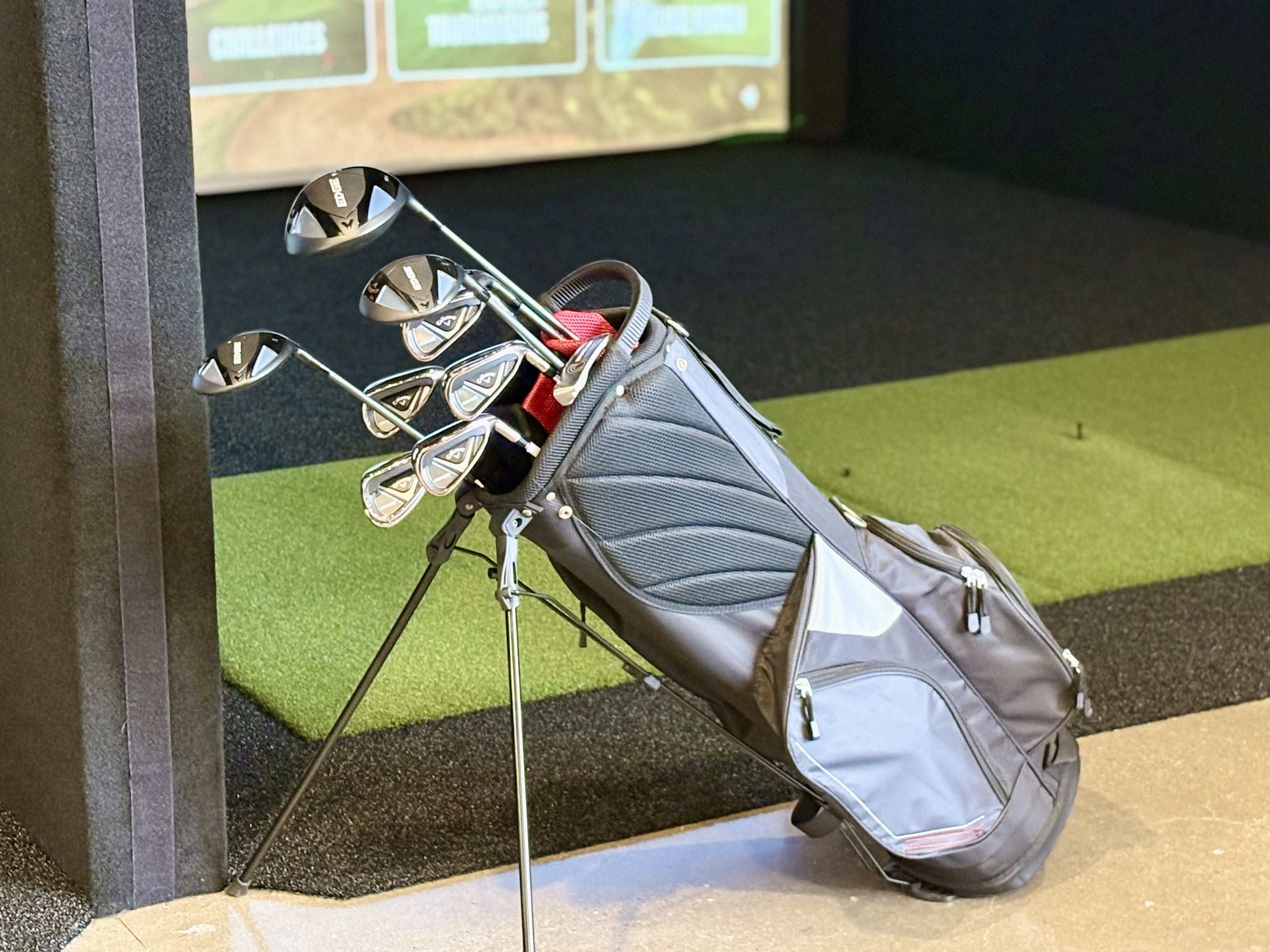 Golf bag with clubs beside the hitting area inside a GridZone indoor golf simulator bay.