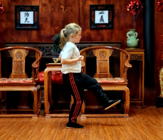 Young girl practicing martial arts indoors, lifting one leg with fists clenched.