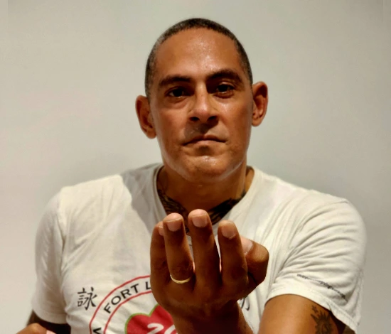 Man in white T-shirt reaching hand toward the camera against a plain background.