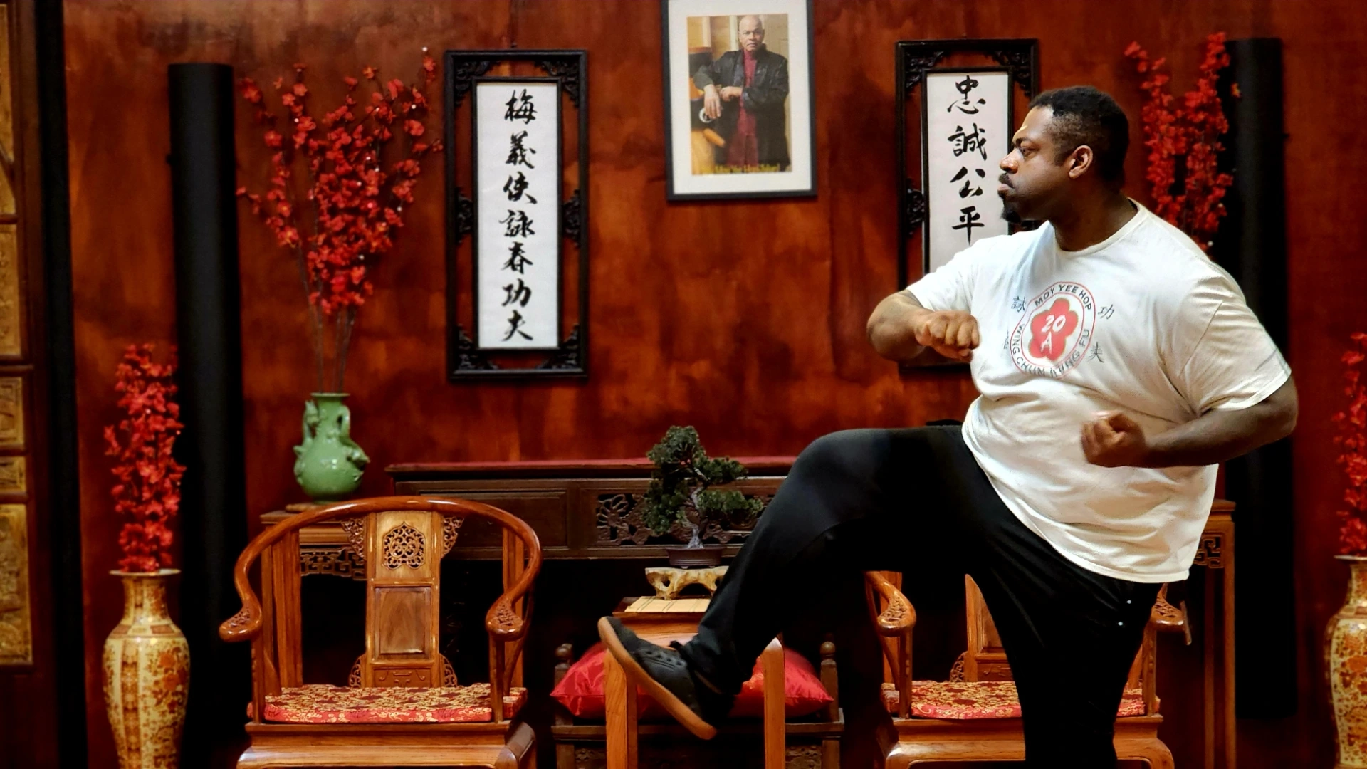 Man in white shirt executing a low martial arts kick inside a traditional studio.