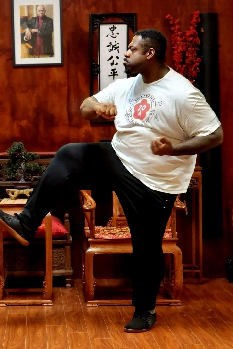 Man in white shirt executing a low martial arts kick inside a traditional studio.