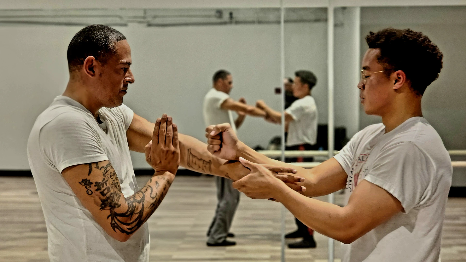 Two men practicing Wing Chun hand drills in front of a studio mirror.
