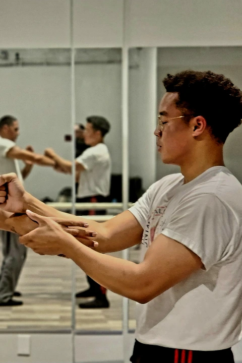 Two men practicing Wing Chun hand drills in front of a studio mirror.