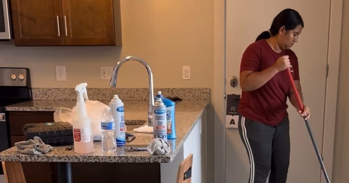 Cleaner mopping beside a kitchen counter lined with cleaning supplies.