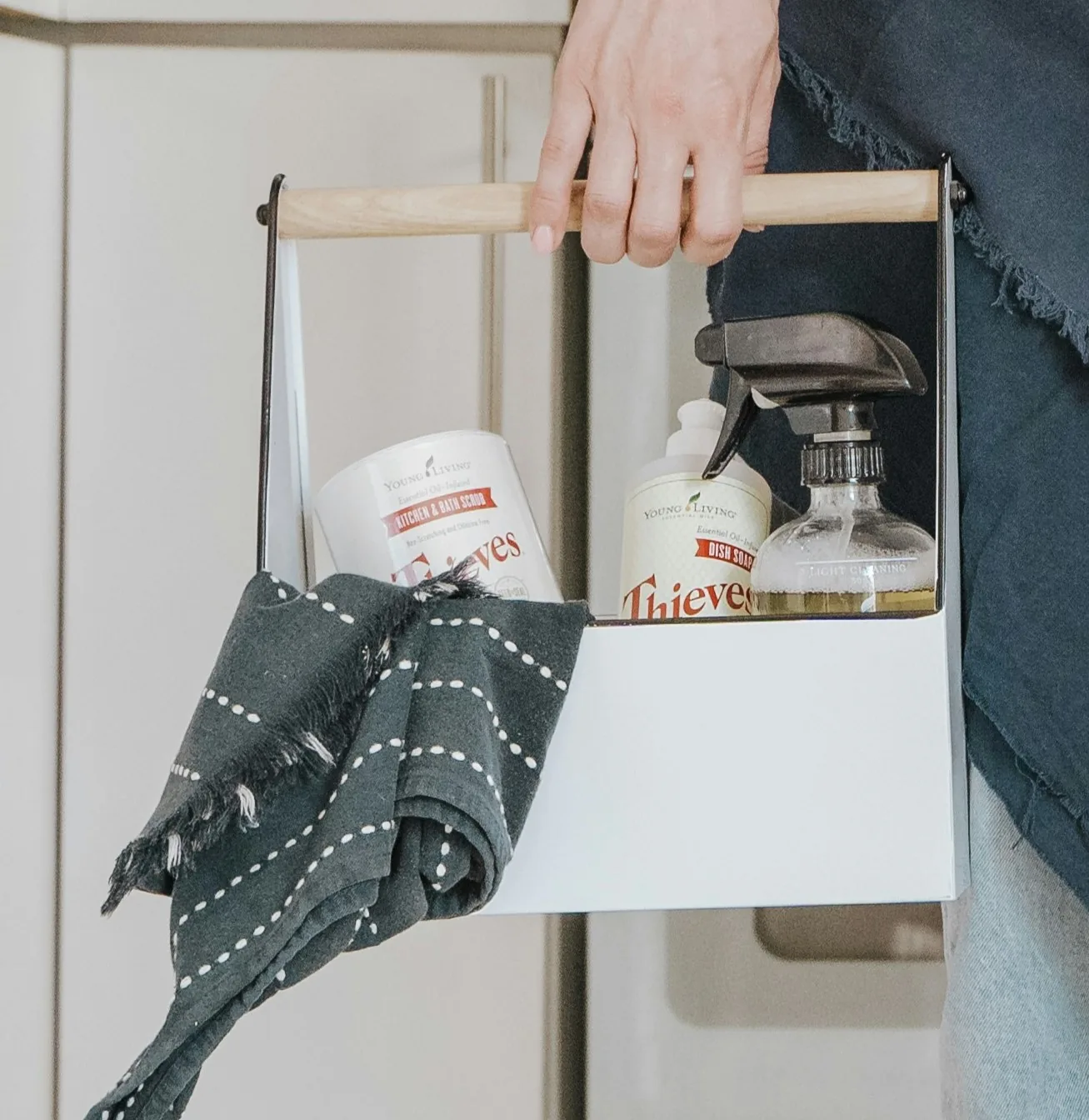Hand carrying a cleaning caddy with spray bottles, supplies, and a cloth.