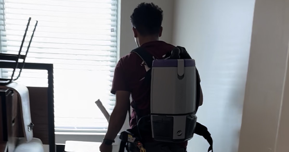 Cleaner wearing a backpack vacuum while cleaning near a window.