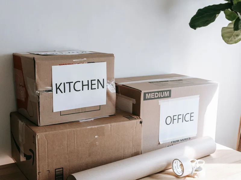 Moving boxes labeled Kitchen and Office stacked on a table with packing paper and tape