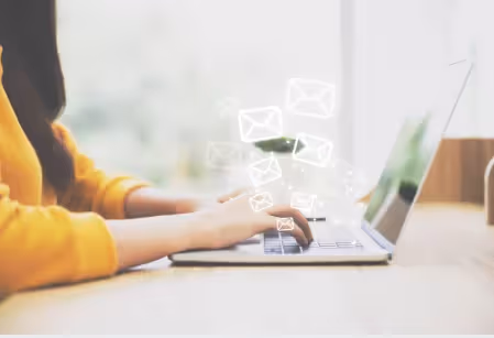A woman typing on a laptop with white envelope icons floating up from the keyboard