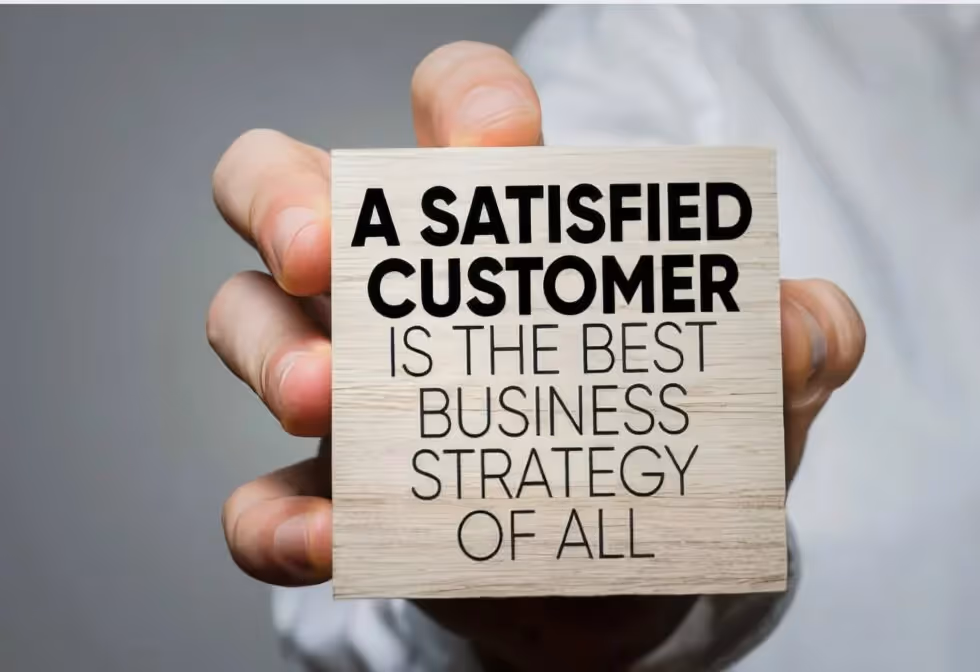 A hand holding a wooden block printed with: A satisfied customer is the best business strategy of all