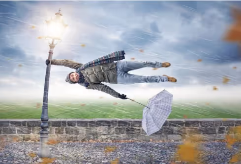 A man blown horizontal by a storm, clinging to a lamppost with his umbrella turned inside out