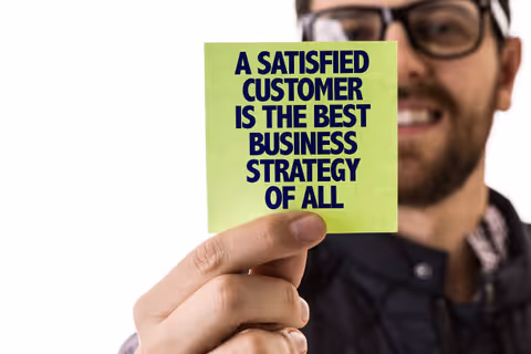 A man holding up a green sticky note reading: A satisfied customer is the best business strategy of all