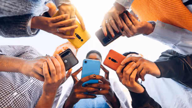 Viewed from below, a circle of people each holding a brightly coloured smartphone