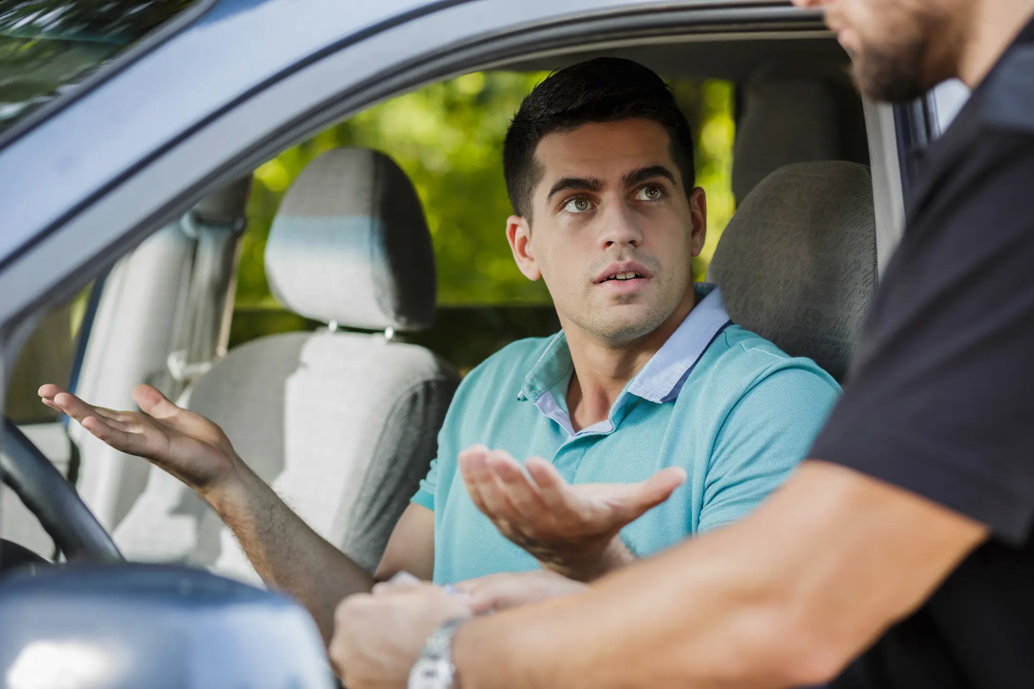 A driver gesturing as he speaks with a police officer standing at his car window