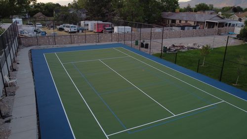 Empty outdoor tennis court with green surface, blue border, and white and blue court lines.