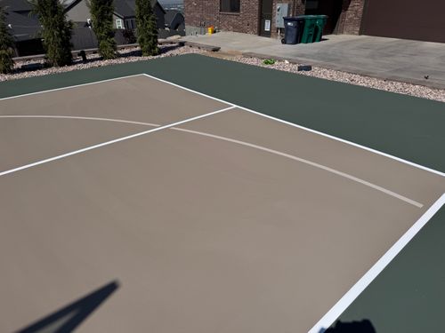 Partial outdoor basketball court with beige playing area, green border, and white boundary lines.