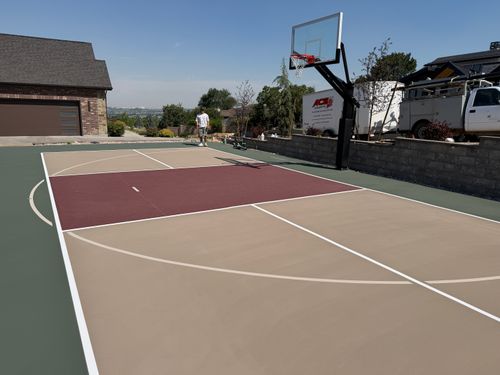 Outdoor residential basketball court with a multi-colored painted surface and single hoop.