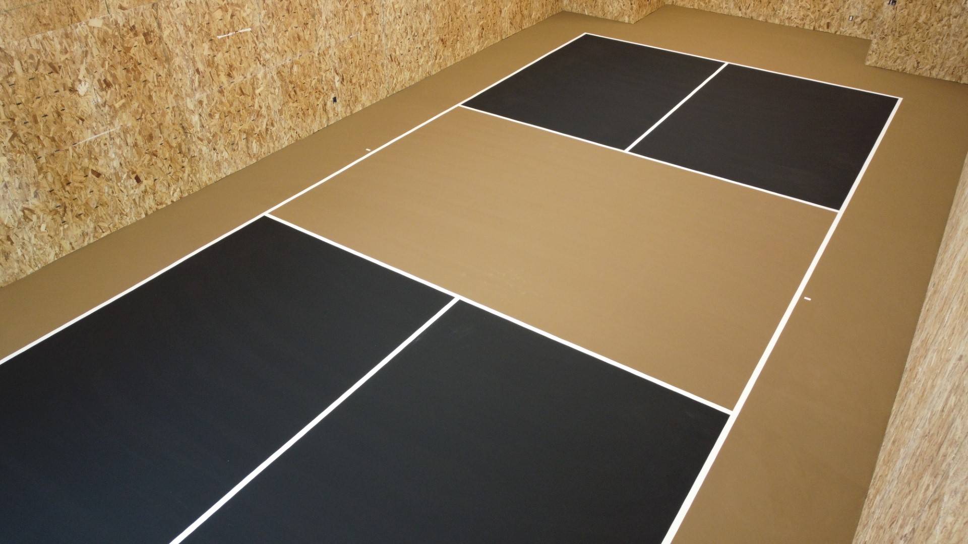 Indoor pickleball court with black and tan floor panels and wood-paneled walls.