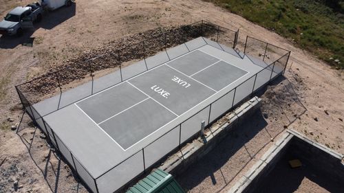 A fenced gray outdoor pickleball or tennis court with the word LUXE painted in the center.