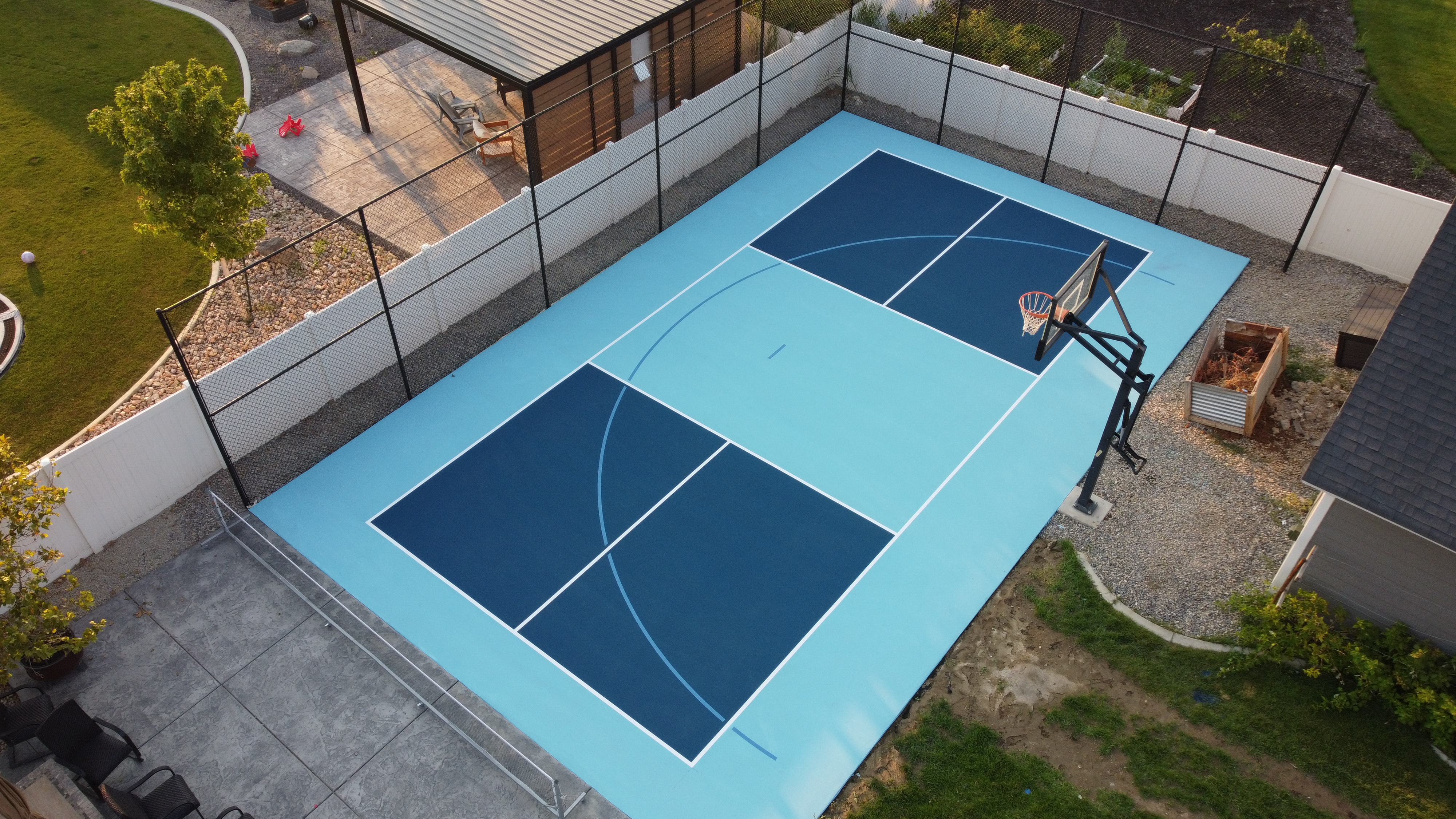 Aerial view of a private backyard basketball court with a blue playing surface and a hoop.