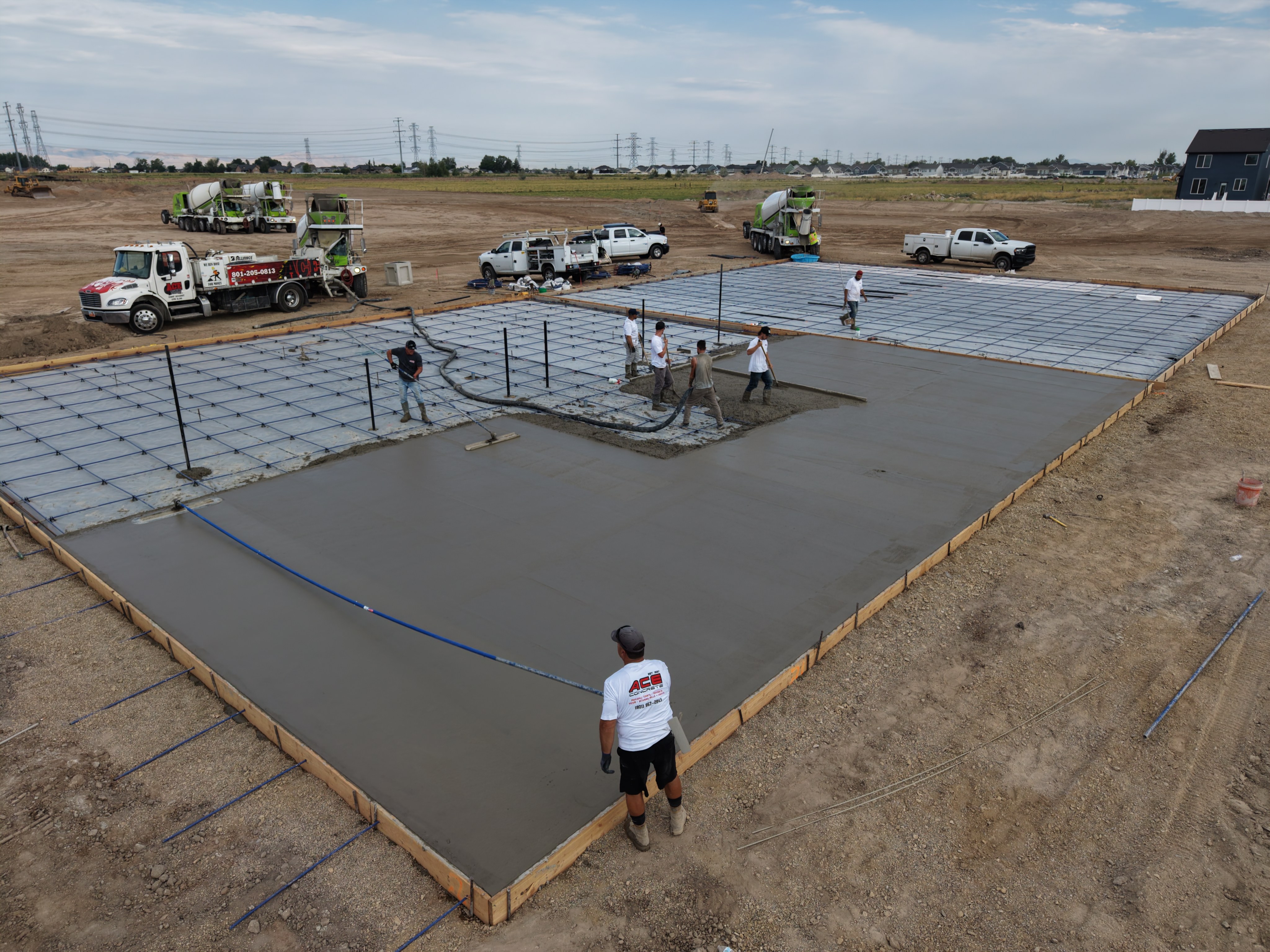 Crew placing and finishing a large concrete court slab, with construction trucks and equipment around the site.