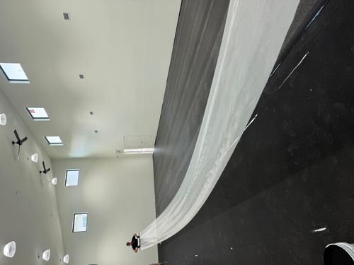 Long strip of white material laid across a dark indoor court floor during surface installation.