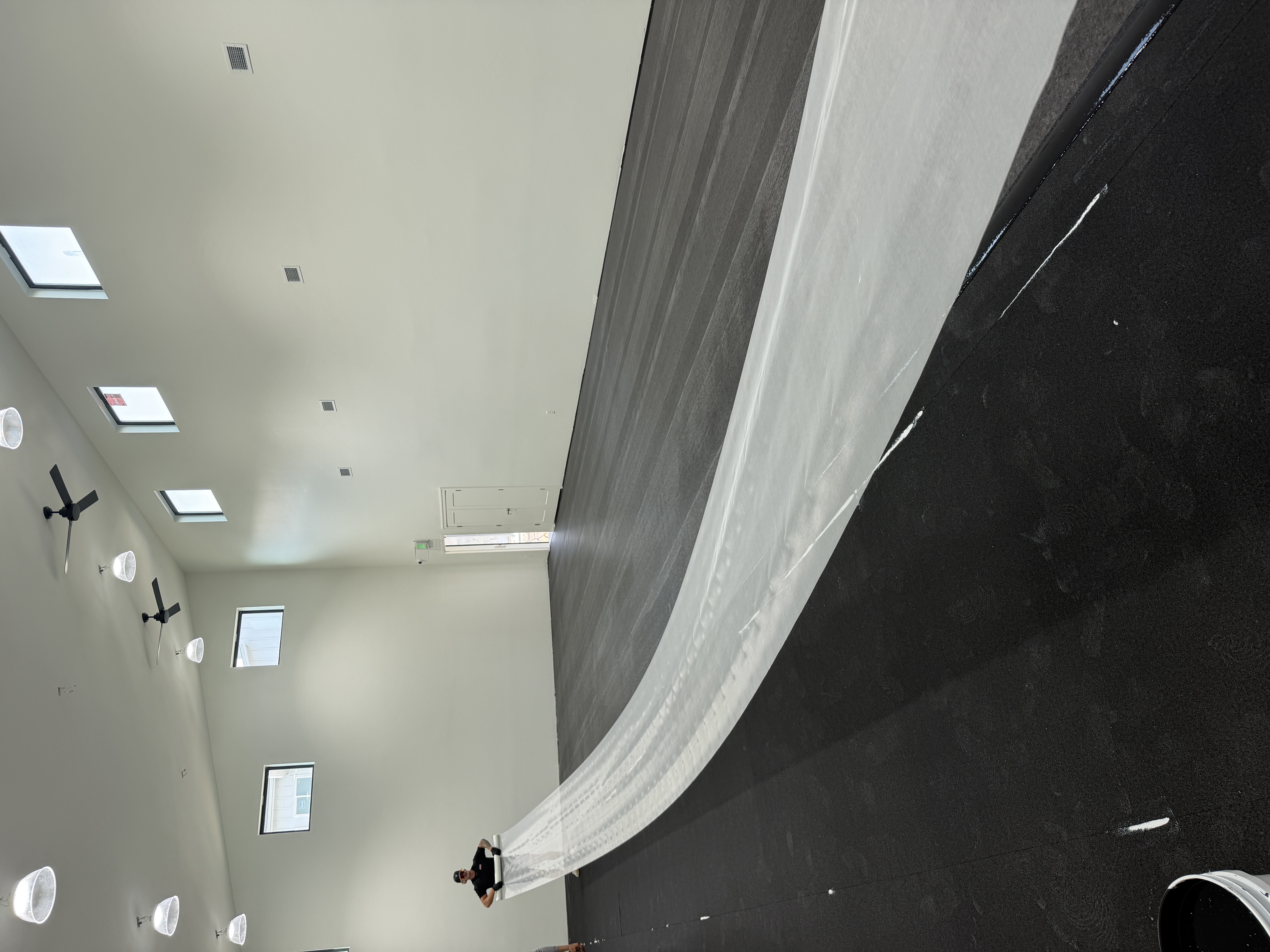 Long strip of white material laid across a dark indoor court floor during surface installation.