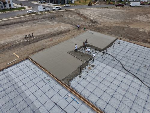 Crew pouring and leveling concrete for a court slab, with a pump hose and reinforcement grid visible.