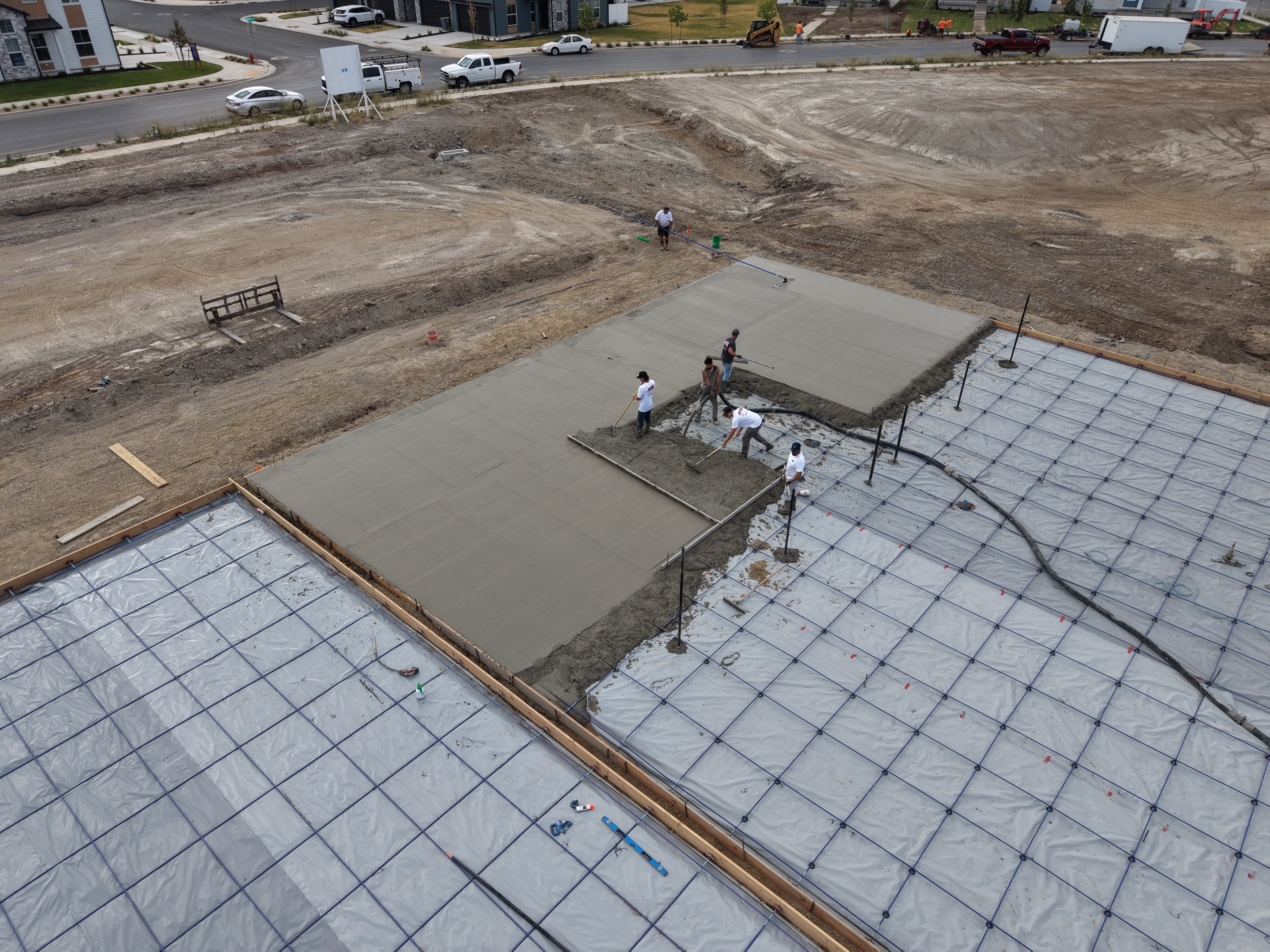 Crew pouring and leveling concrete for a court slab, with a pump hose and reinforcement grid visible.