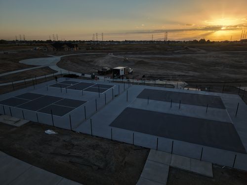 Fenced outdoor court complex at sunset, with multiple playing areas and paved walkways across an open site.