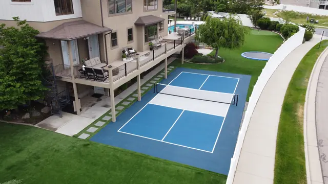 Blue backyard court with a light center section beside a lawn and curved path.
