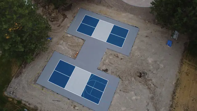 Aerial view of two blue playing areas connected by a gray court surface.