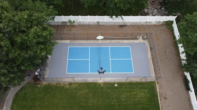 Blue outdoor court with white game lines, a gray border and a basketball hoop.