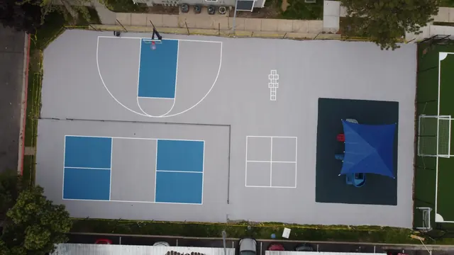 Blue and gray recreation area combining a net court, basketball hoop and playground.