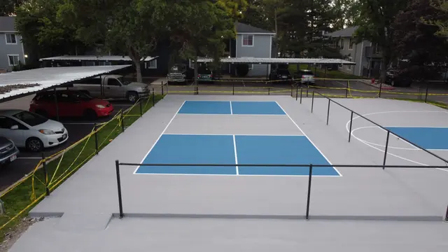 Blue and gray recreation area combining a net court, basketball hoop and playground.