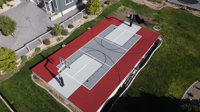 Aerial view of a red and gray backyard basketball court with two hoops.