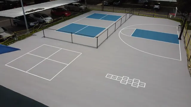 Blue and gray recreation area combining a net court, basketball hoop and playground.