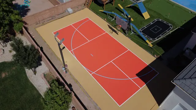 Orange basketball playing area with a tan border beside a backyard play space.