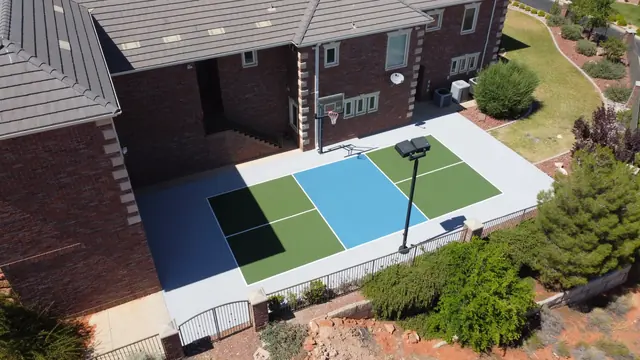 Blue and green basketball half court beside a brick home.
