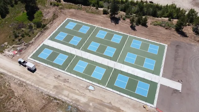 Overhead view of multiple blue and green pickleball courts arranged around walkways.