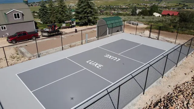Gray outdoor court with white markings and perimeter fencing.