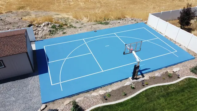 Blue backyard basketball court bordered by a lawn and rock landscaping.